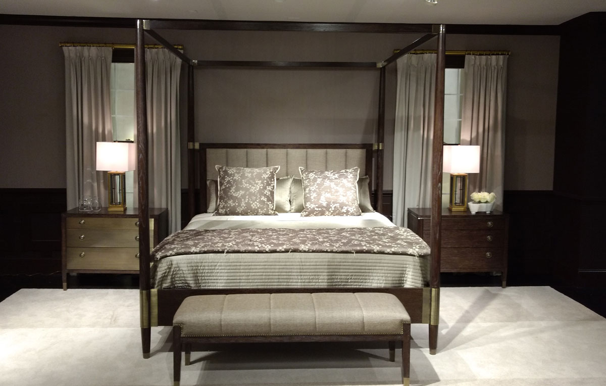 Four post framed bed covered in gray linens against gray walls with gray drapes.